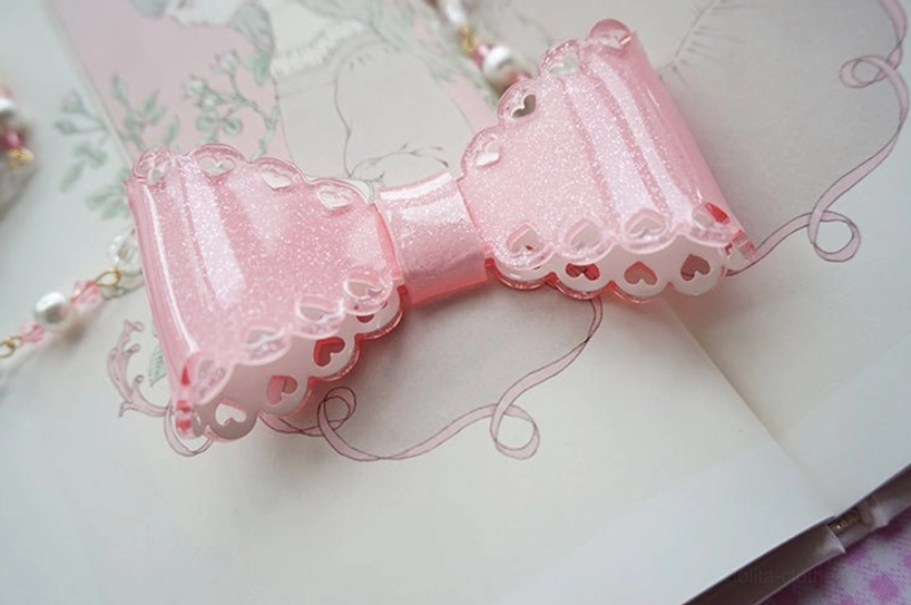 Shiny glittery pink scalloped edge resin bow necklace with delicate beaded chain close-up shot low-angle vintage book background