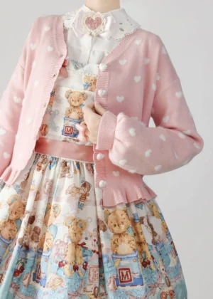 Pink heart-patterned sweet lolita cardigan sweater with white heart jacquard, ruffled hem, pearl buttons, and bishop sleeves displayed on mannequin with teddy bear print dress and lace collar blouse