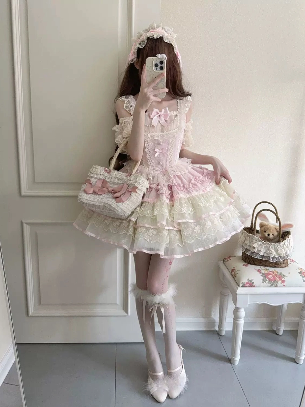 Front mirror selfie wearing pink and ivory sweet lolita JSK dress with matching hair accessory, ruffled sleeveless bodice, pink bust bow, layered lace petal skirt, and coordinating lolita handbag