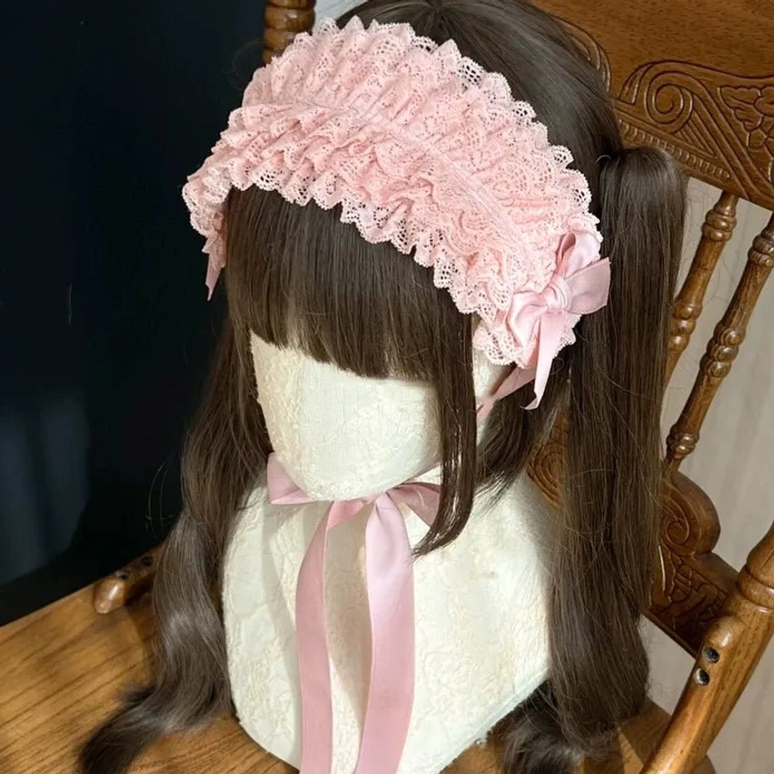 Elegant pink ruffled lace KC headdress worn on mannequin with brown twin ponytails, featuring side satin bow and flowing neck ribbon on vintage wooden backdrop