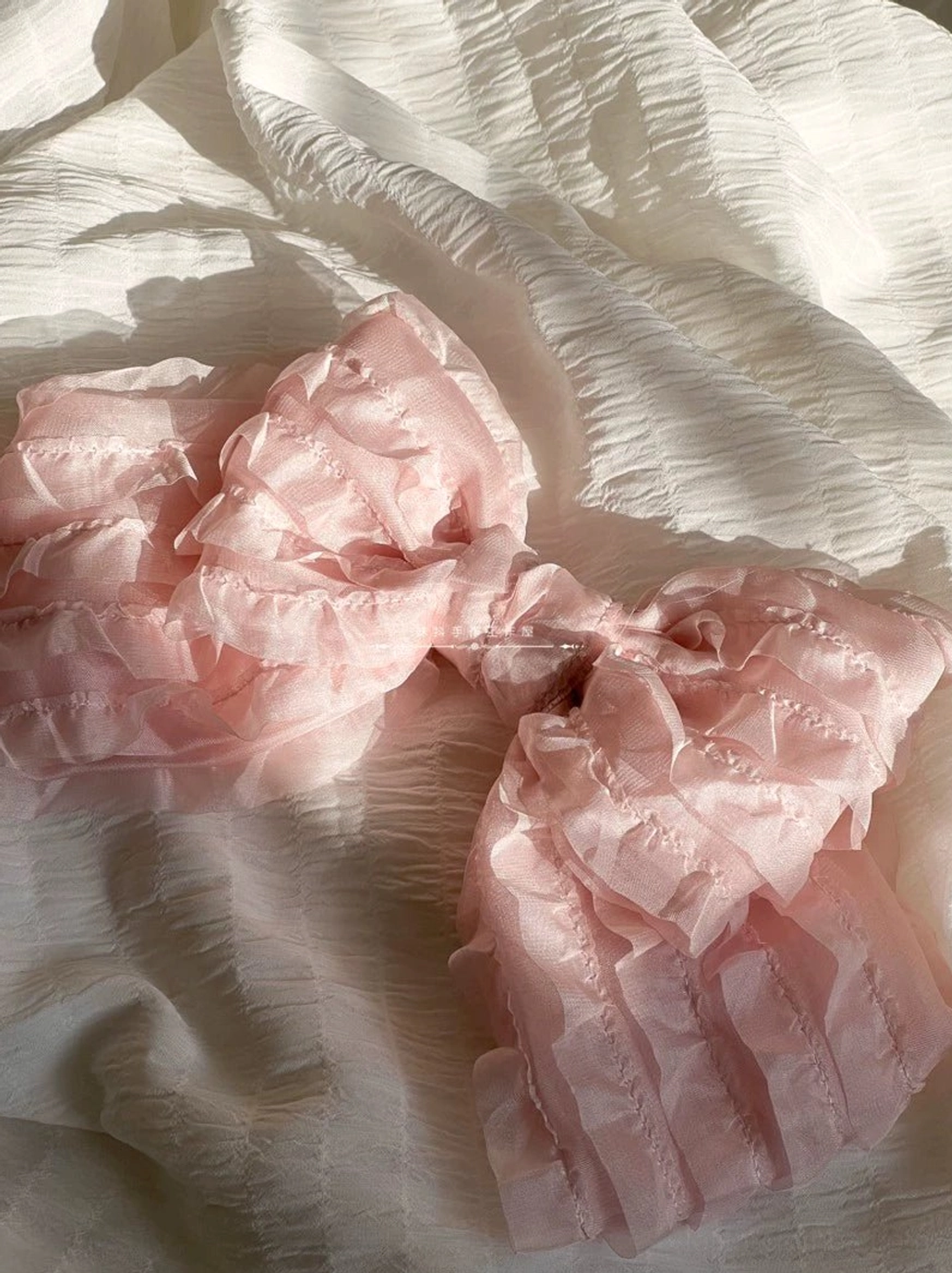 Single pink layered ruffled organza bow lolita hair clip flat lay top-down view on white wrinkled fabric