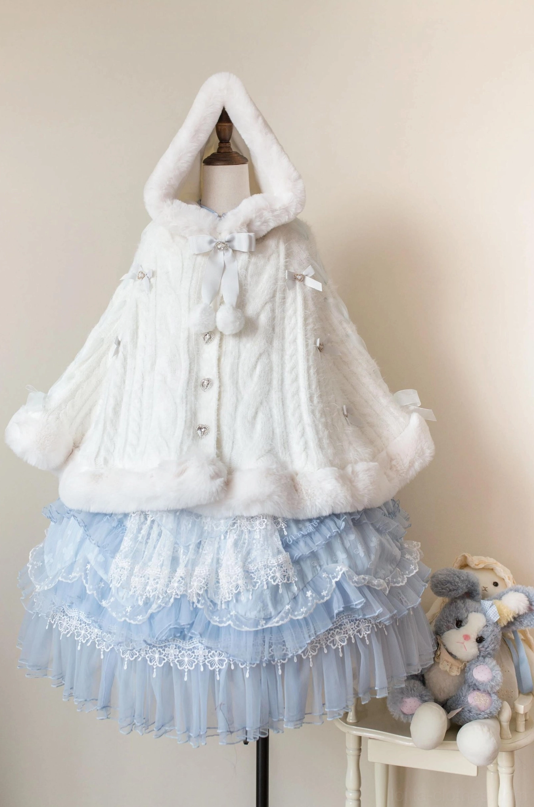 Pink lolita winter cape coat featuring cable knit texture and decorative pom-pom accents, coordinated with pink tiered ruffled skirt for classic sweet lolita look