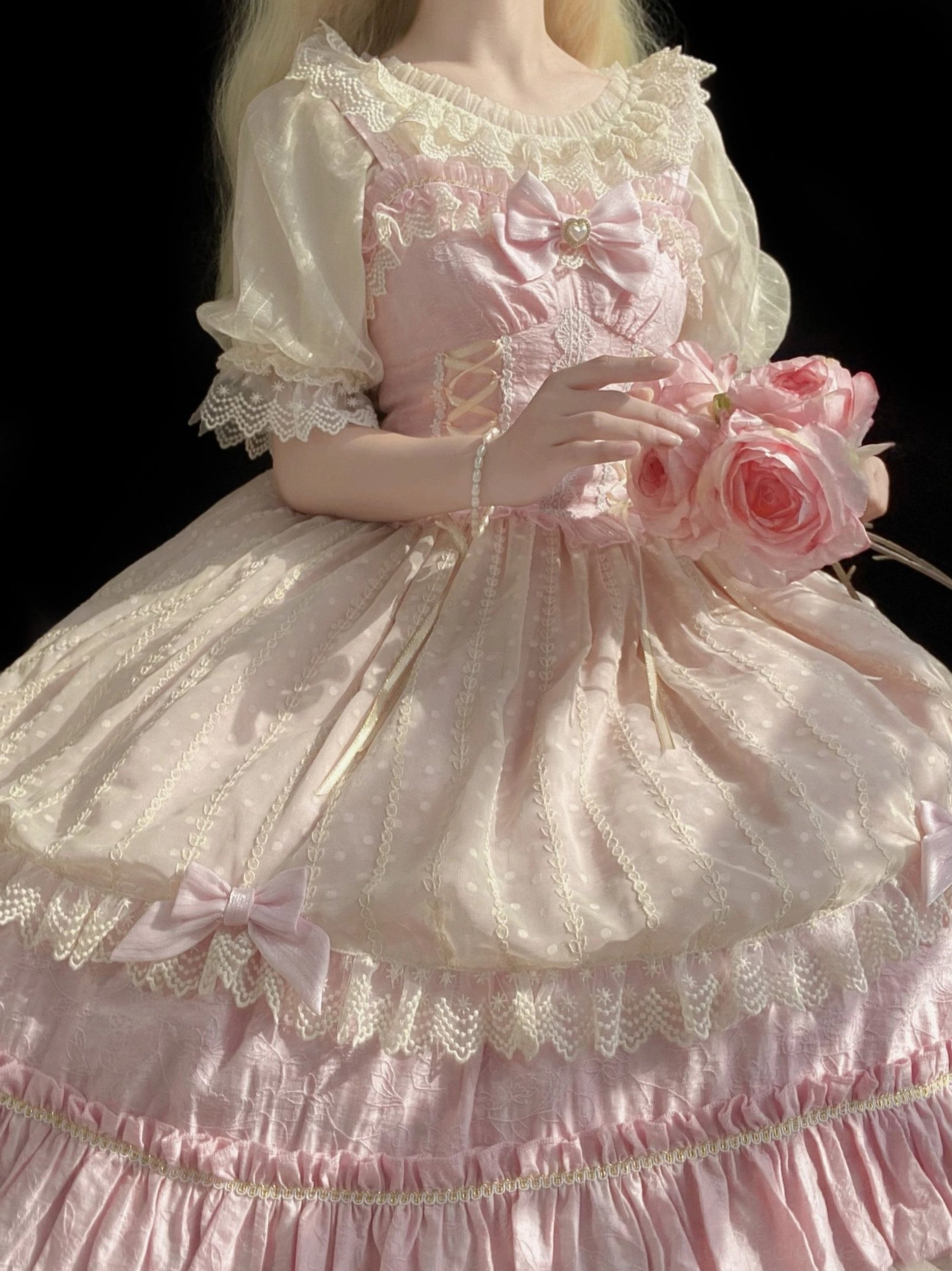 Close-up front detail shot of pink sweet Lolita dress featuring dotted shiny chiffon fabric, corset lacing details, front bow, and layered ruffled lace skirt