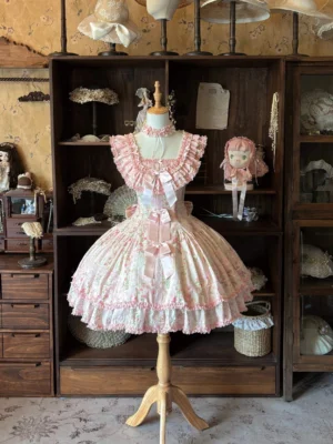 Straight front view of pink rose print Lolita jumper skirt dress showing ruffled square collar, layered frill trim, and full gathered skirt silhouette on vintage wooden shelf