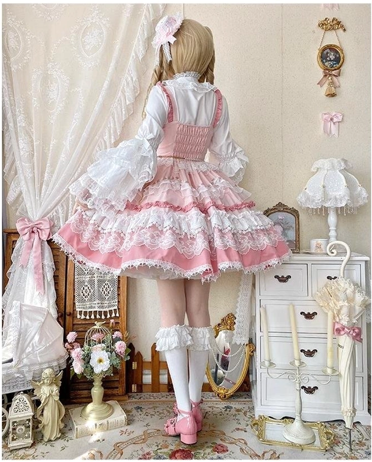 Back view of pink sweet lolita JSK dress on blonde twin-braid model showing adjustable shoulder straps, white lace inner blouse, pink hair bow and layered lace