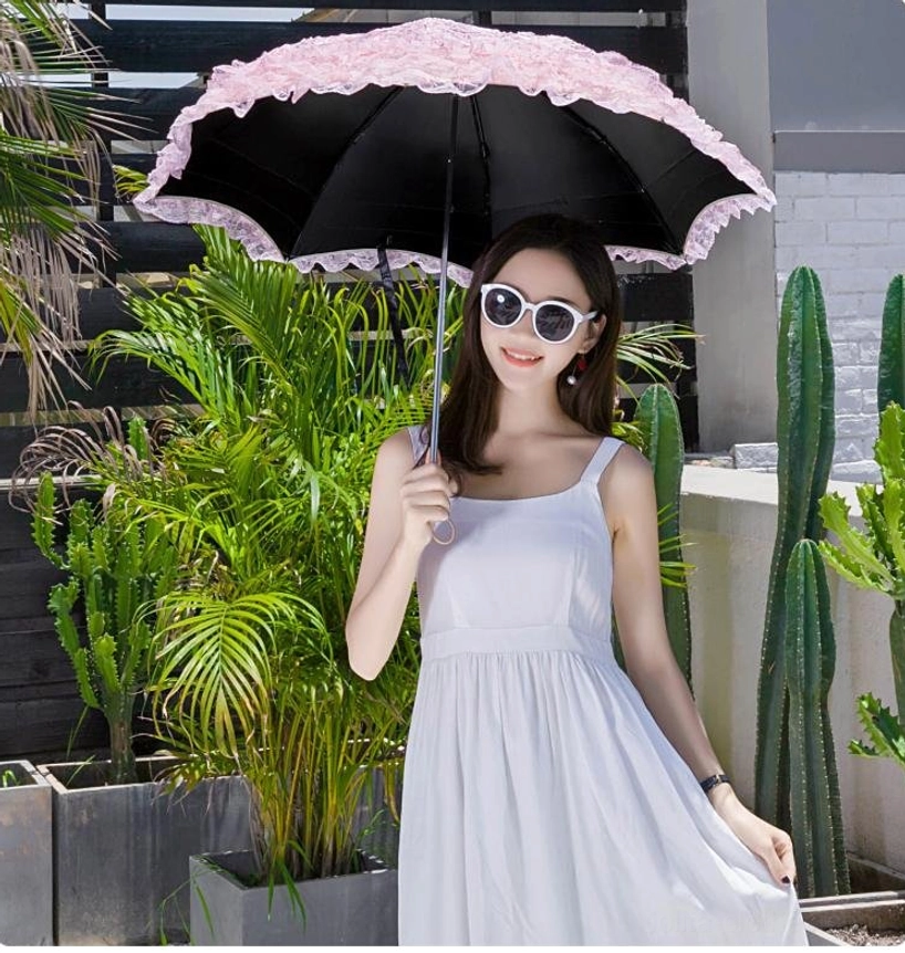 Woman wearing sunglasses holding pink lace Lolita parasol with black inner UV-protective lining, front view on tropical outdoor balcony with green plants