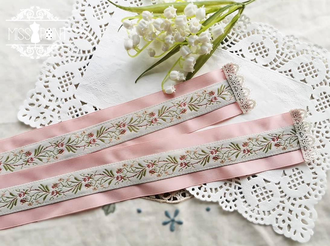 Flat lay photography of pink satin lolita ribbon belt with delicate floral weaving and pearl embellishments on lace doily background