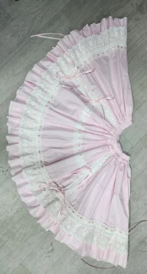Pink lolita underskirt flat lay overhead view showing full circle flare silhouette elastic waistband white lace details and ruffled hem bottom edge