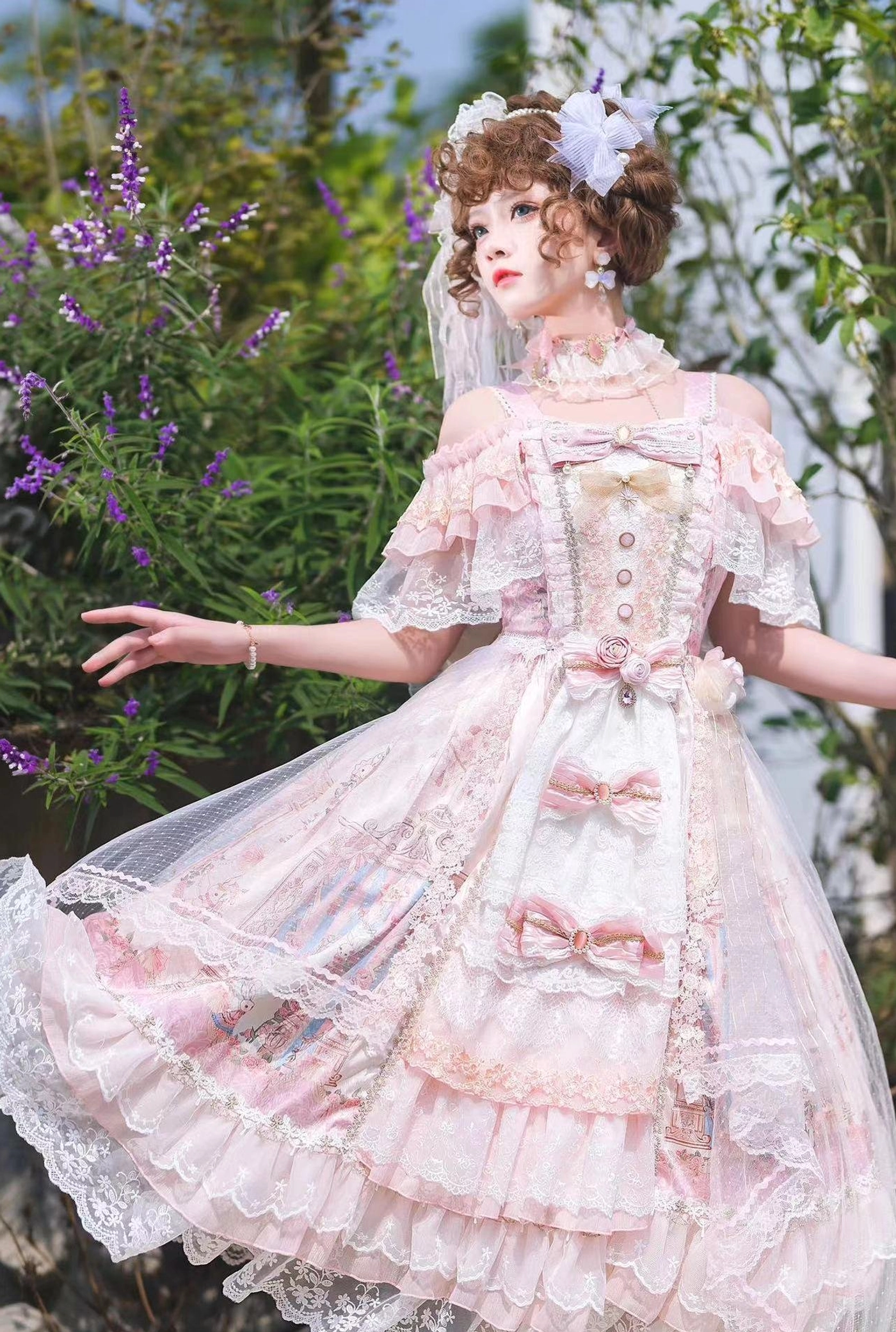 Pink off-shoulder wedding Lolita JSK dress with ruffled lace sleeves and layered tulle skirt, model wearing floral hair ornaments in lavender garden setting