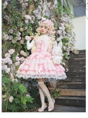 Pink old school lolita jumper skirt with tiered lace ruffles and satin bow on blonde model in garden setting