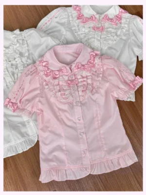 Pink old school lolita blouse with peter pan collar and delicate pink bow chest panel displayed with white variant on wooden table flat lay