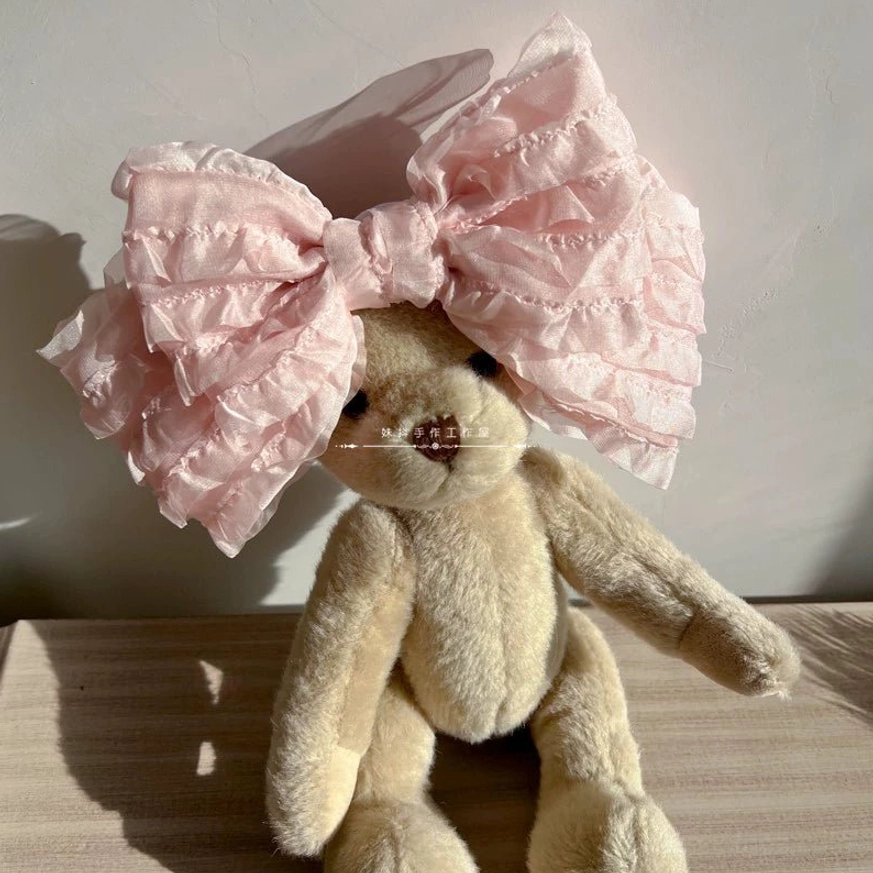 Pink ruffled organza lolita hair clip side oblique angle view on teddy bear prop wooden table backdrop