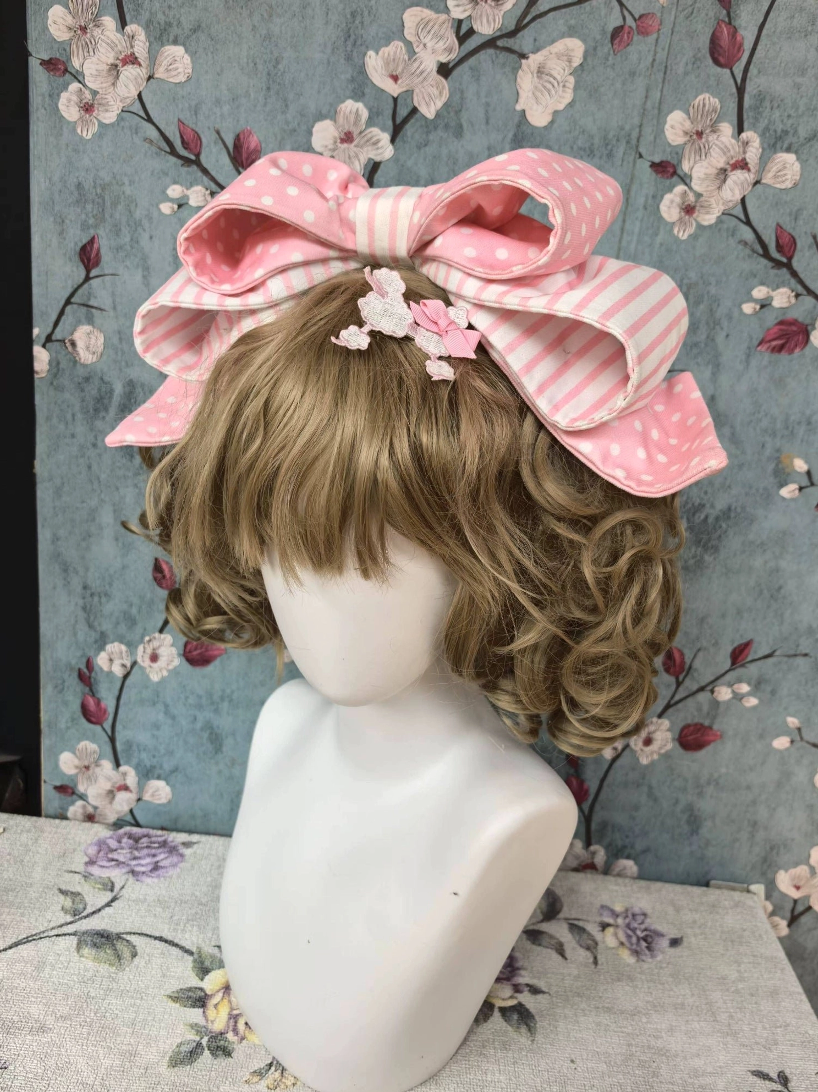 Pink polka dot lolita KC headbow with big double-layer bow featuring polka dot and stripe fabric, coordinating with curly blonde wig and lolita ensemble