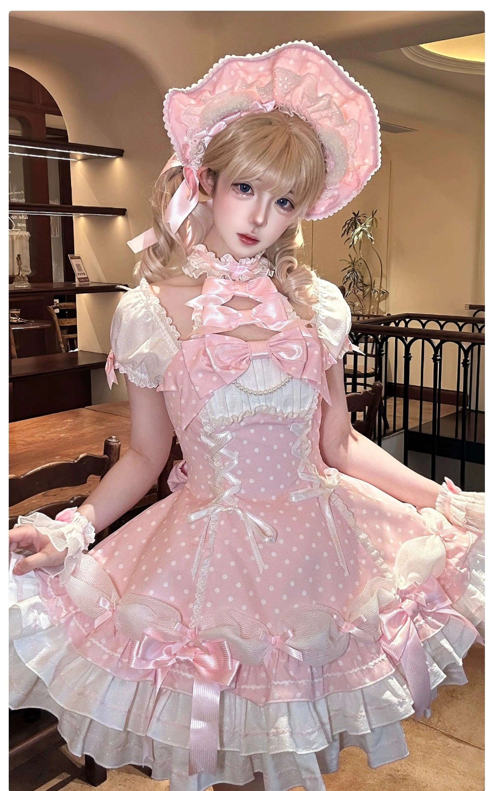 Pink polka dot off-shoulder Lolita OP dress model front view with matching bonnet cuffs layered ruffles vintage cafe environment
