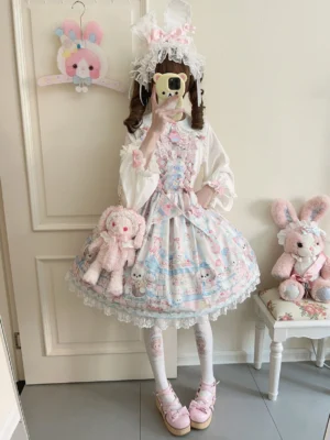 Pink sweet Lolita coordinate complete outfit including puppy print JSK jumper skirt with matching sash, shown on girl in back mirror view wearing hair accessories and holding pink plush handbag in cozy room