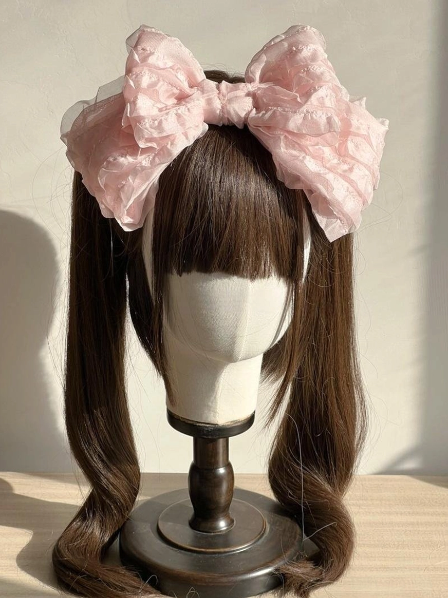 Oversized ruffled organza pink bow lolita hair clip close-up front view on mannequin with twin-tailed brown curly wig and wooden display stand