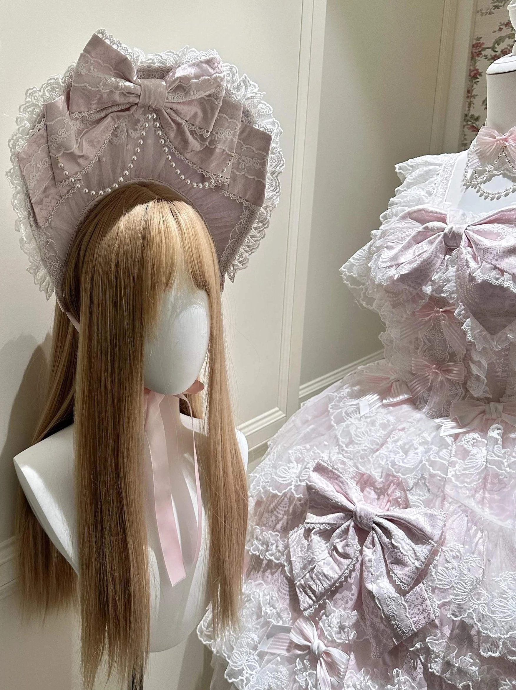 Partial close-up front view of pink Sakura Blossom Dream Sweet Lolita accessory ensemble featuring pearl-trimmed pink bonnet with lace ruffles, pink satin bows with decorative lace edging, pink coordinating choker necklace, tiered tulle and lace skirt construction, showcasing ornate Sweet Lolita romantic aesthetic details