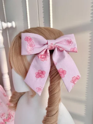 Pink sakura cherry blossom bow hair clip rear back view worn on blonde mannequin with twin ponytails showing delicate floral print and large bow shape