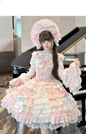 Pink Sakura Love lolita dress suit front three-quarter view with tiered ruffle skirt, extensive lace trim, statement bow bonnet, and decorative pearls, modeled indoors at grand piano