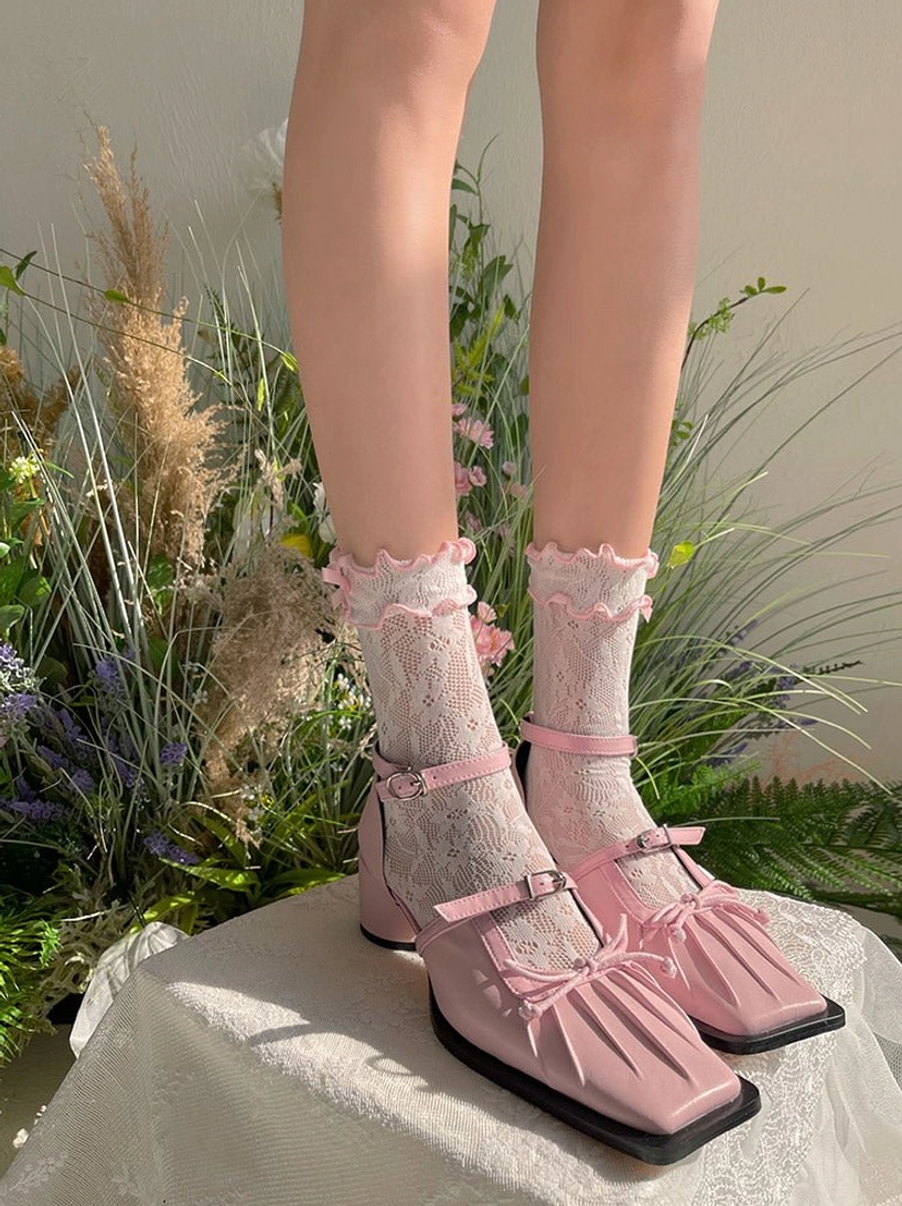 Pink sheer floral lace ankle socks with ruffled cuff paired with coordinated pink square-toe Mary Jane Lolita shoes displayed on model's feet with greenery backdrop