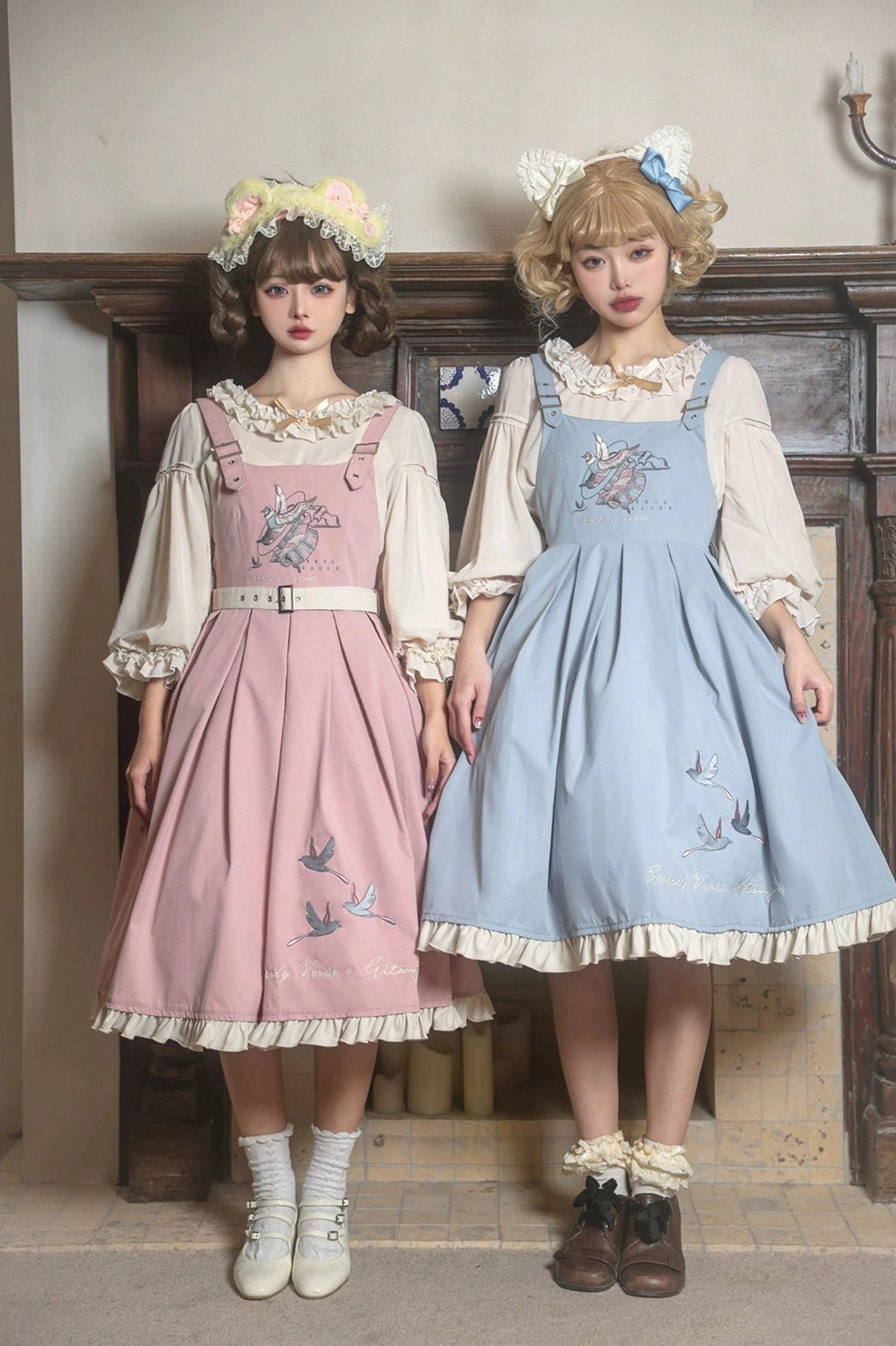 Pink and sky-blue bird embroidery Lolita JSK dresses with inner blouses dual model display front standing view indoor retro wooden doorway background coordinated aesthetic