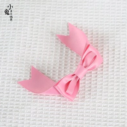 Small pink split-tail bow hair clip top-down flat lay view showing solid color satin fabric and classic lolita bow shape
