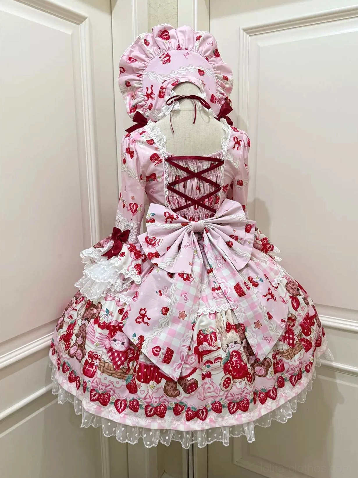 Pink sweet lolita OP dress back view on mannequin displaying crisscross lace-up back, soft pink satin waist bow, layered ruffled skirt, strawberry bear prints and white lace details