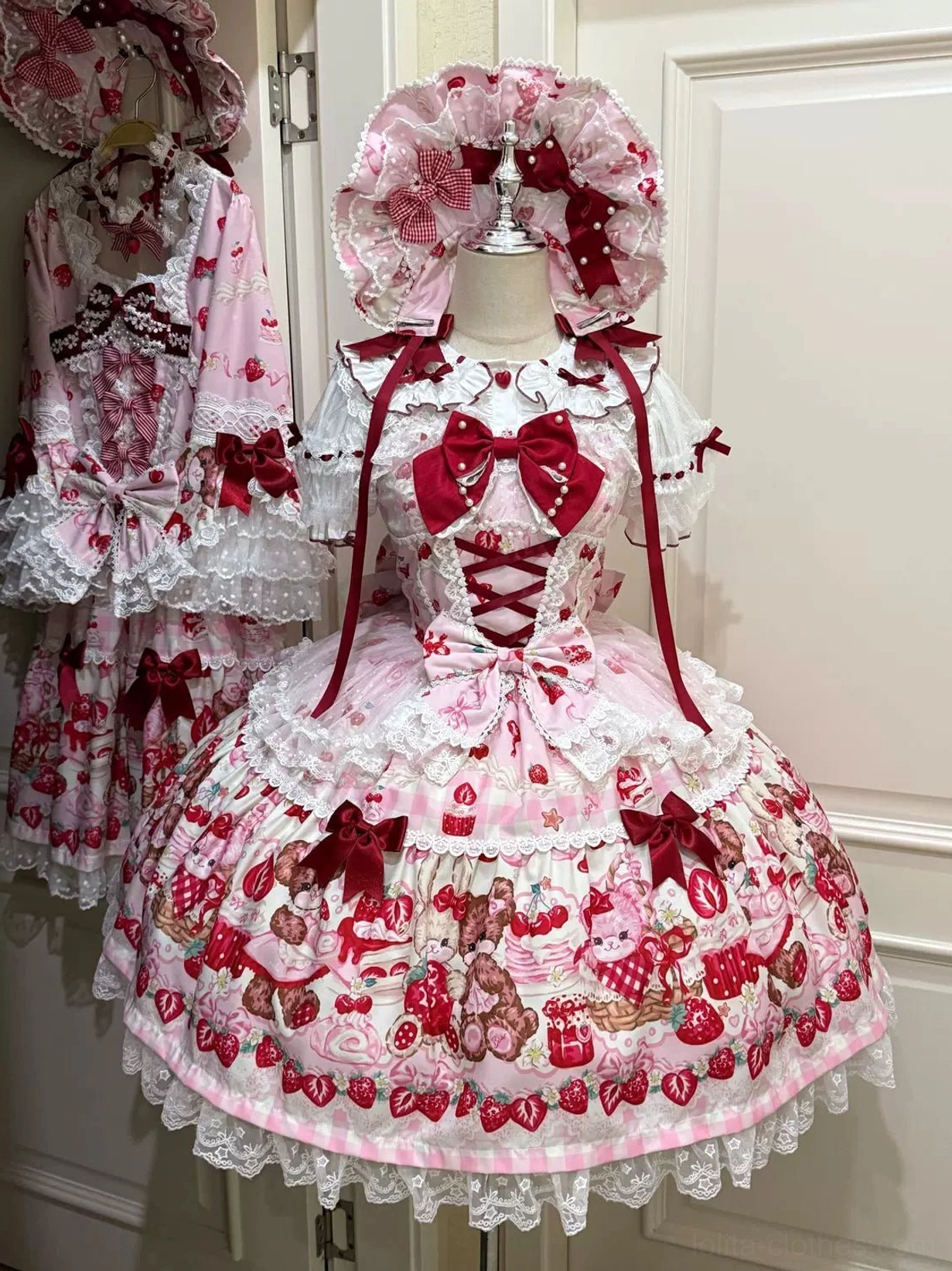 Pink base strawberry bear print sweet lolita JSK dress front view with red bow ribbon accents and lace-up bodice