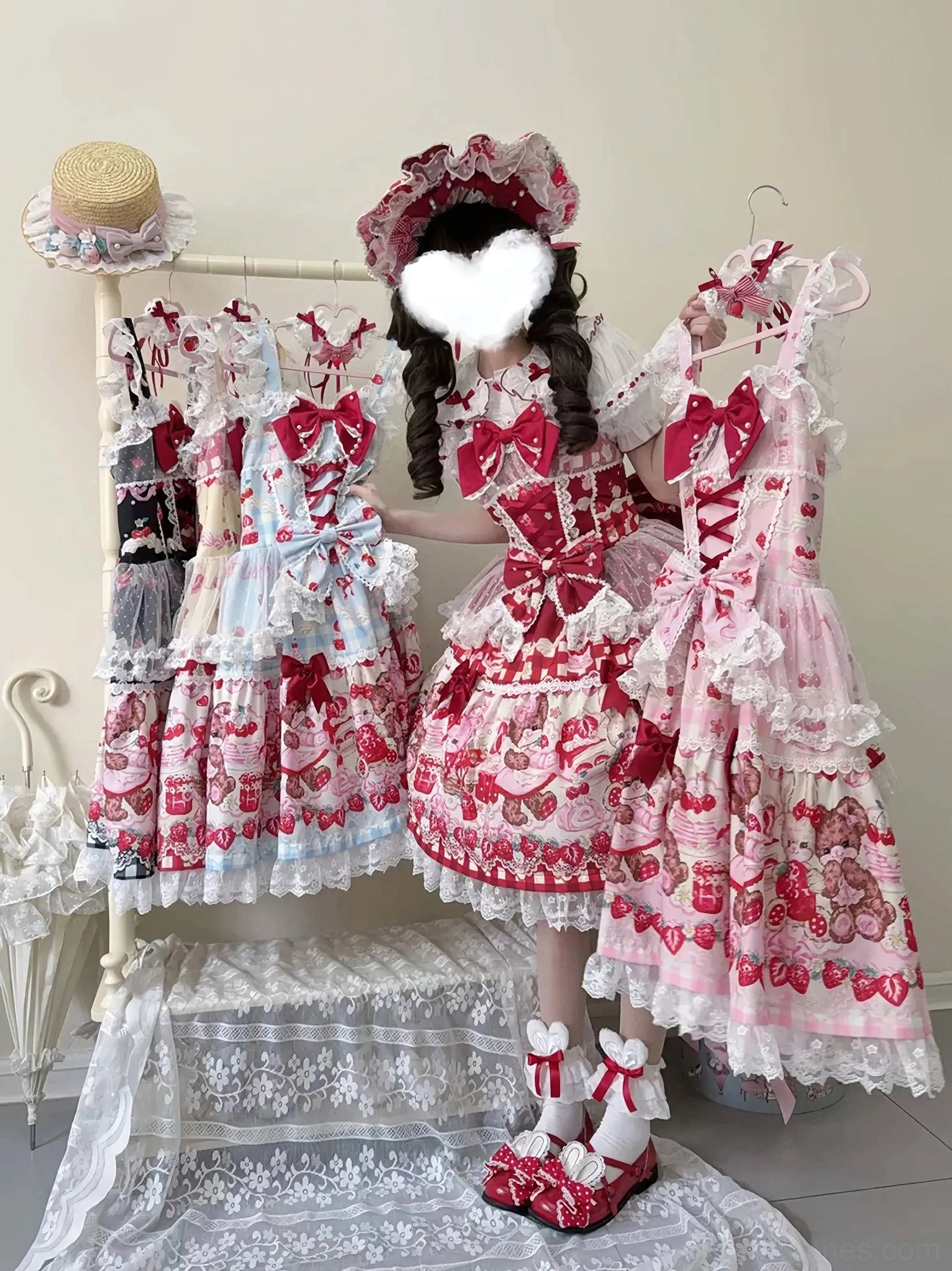 Pink strawberry print sweet lolita JSK dress worn by model in boutique setting with ruffled straps and matching bonnet
