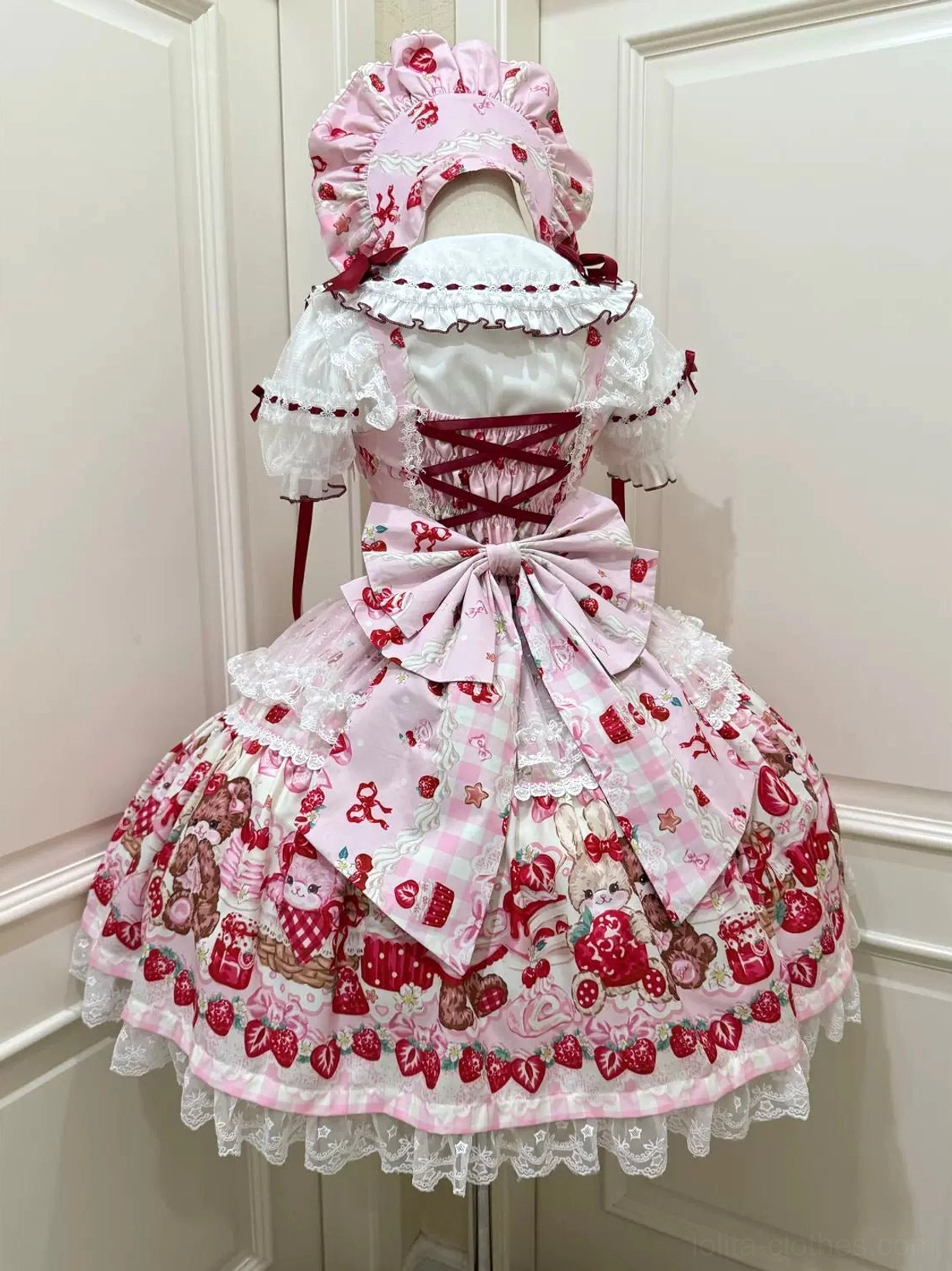 Pink strawberry print sweet lolita JSK dress back view with pink trailing bow and lace-up bodice on dress form