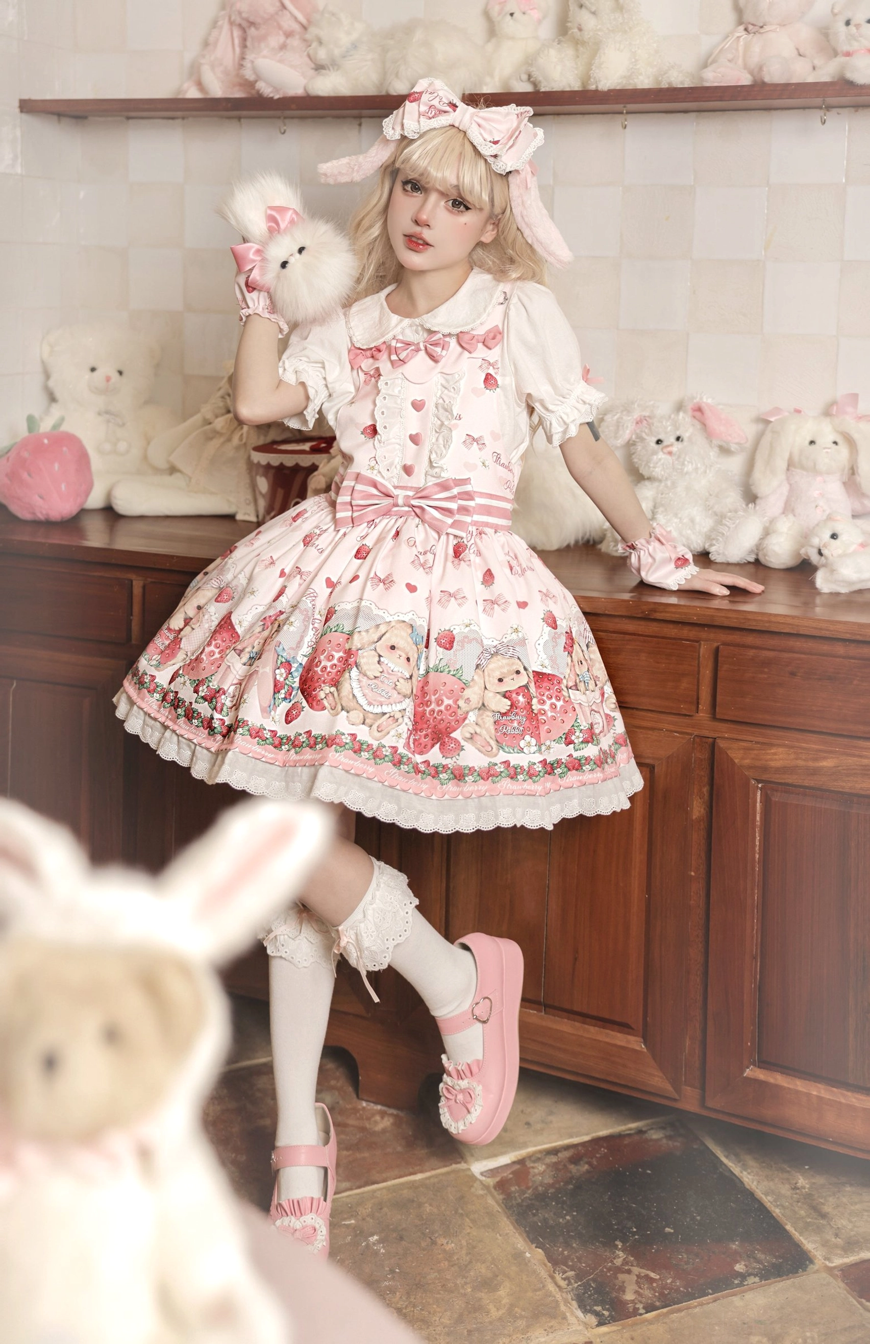 Full body pink strawberry sweet lolita salopette dress worn by blonde model with bunny ear hair clips peter pan collar and ruffled lace hem