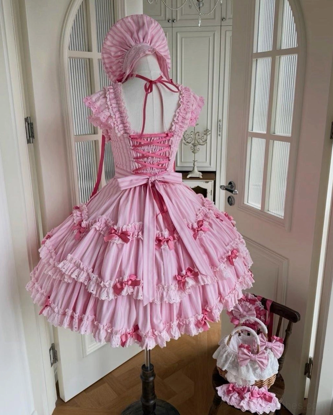 Back view of pink striped Lolita jumper skirt dress showing lace-up closure, large waist bow, and layered ruffled tiered skirt design