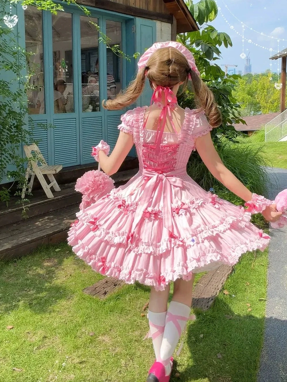 Back full-body outdoor shot of pink striped classic Lolita jumper skirt with twin tails hairstyle, striped knee socks, and Mary Jane shoes
