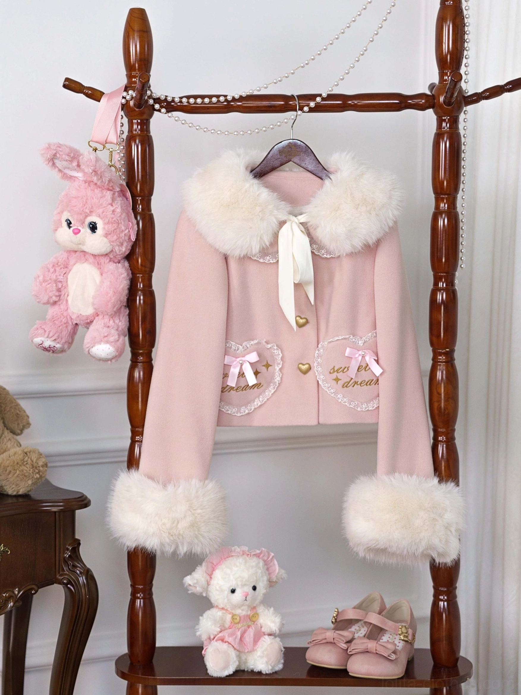 Pink fleece-lined sweet lolita coat with detachable faux fur collar and cuffs, lace-trimmed heart pockets, and satin neck bow, displayed overhead on vintage styling props