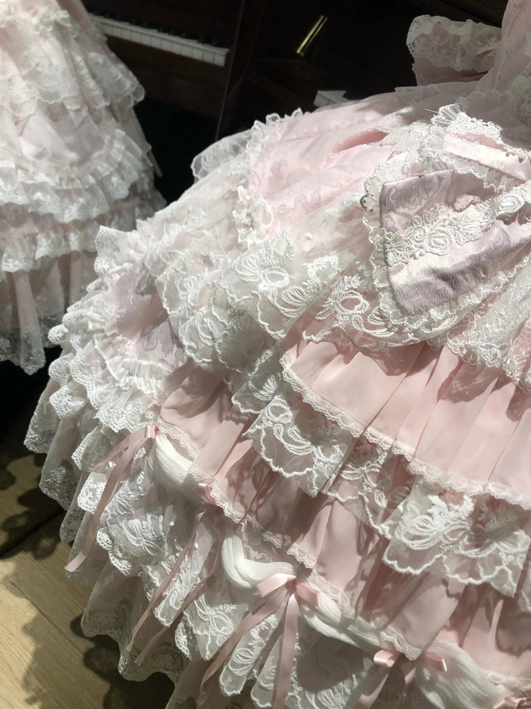 Close-up detail of pink sweet lolita tiered dress skirt showing white lace trims small pink bows on tiers delicate lace patterns