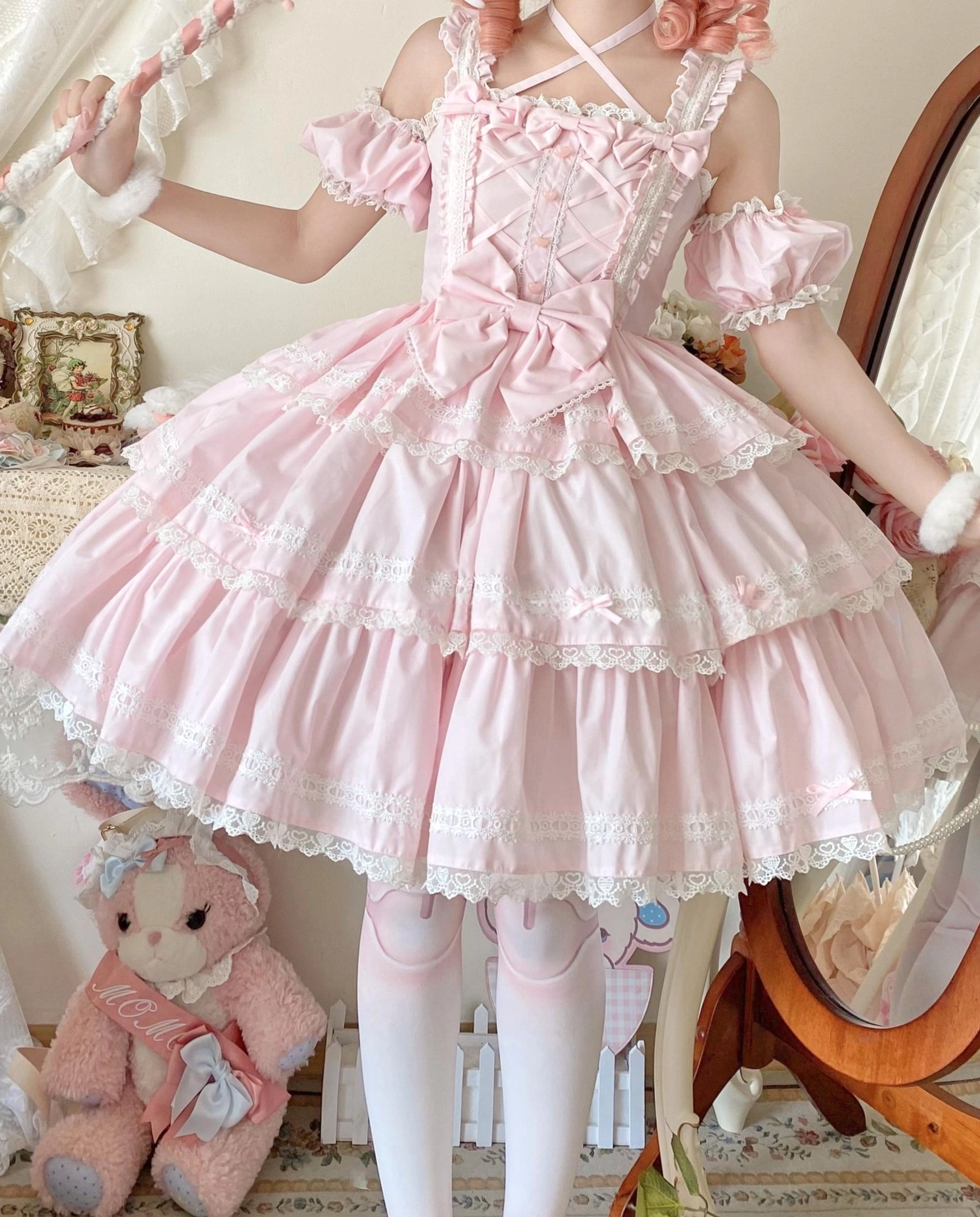 Pink Sweet Lolita JSK dress on cosplay model with plush teddy bear off-shoulder ruffled sleeves crisscross front straps layered lace skirt