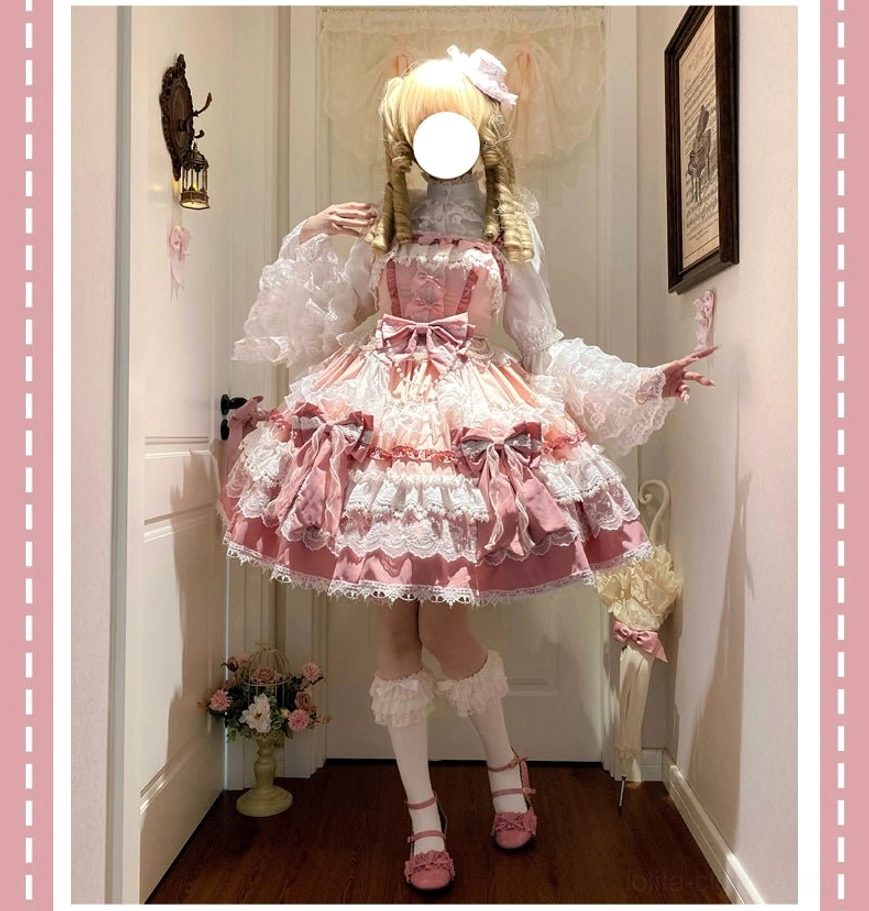 Side back view of pink sweet lolita jumper dress on blonde twin-braid model in hallway showing pink hair bow, layered lace skirt, matching footwear and stockings