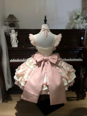 Back view of pink lolita JSK dress showing large detachable satin bow halter strap ruffled shoulder edges tiered lace trimmed skirt vintage piano studio setting
