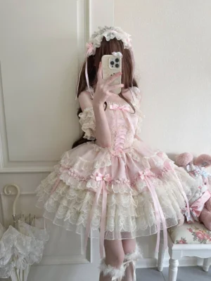 Pink Enchanted Ribbons sweet lolita JSK dress with tiered ruffles and ribbon details, worn with matching flower hair accessory in mirror selfie pose