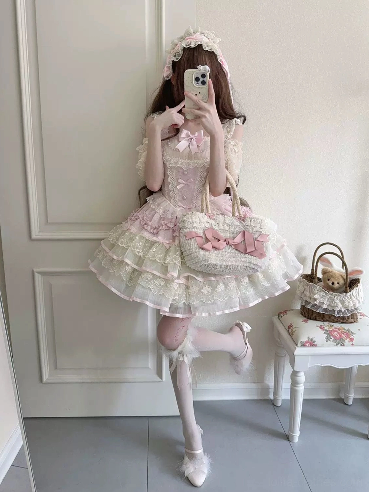 Front mirror selfie with model's leg lifted wearing pink and ivory sweet lolita JSK dress, ruffled neckline, layered lace petal ruffles, matching lolita bag, fluffy leg warmers, and ballet shoes