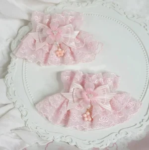pair of pink lolita wrist cuffs with striped satin bow and flower drop pendant displayed on vintage white decorative tray with linen background