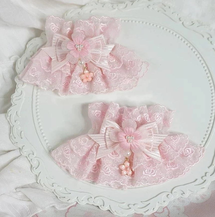 pair of pink lolita wrist cuffs with striped satin bow and flower drop pendant displayed on vintage white decorative tray with linen background