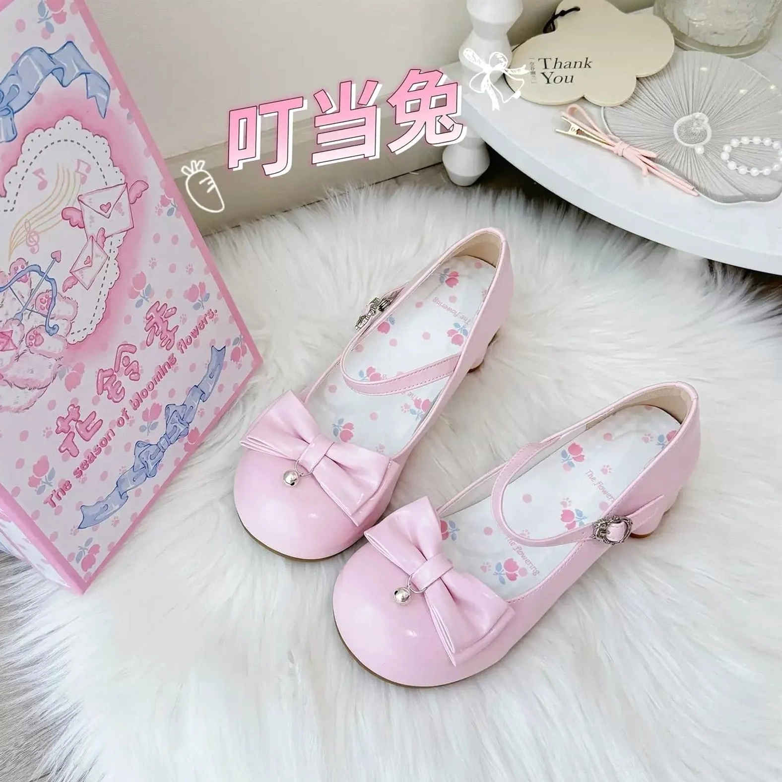 Pink glossy patent leather sweet lolita Mary Jane shoes displayed from side-overhead angle showing patent leather construction, pearl-accented front bow, printed floral inner lining, adjustable ankle buckle strap, and low block heel structure with branded packaging accessories