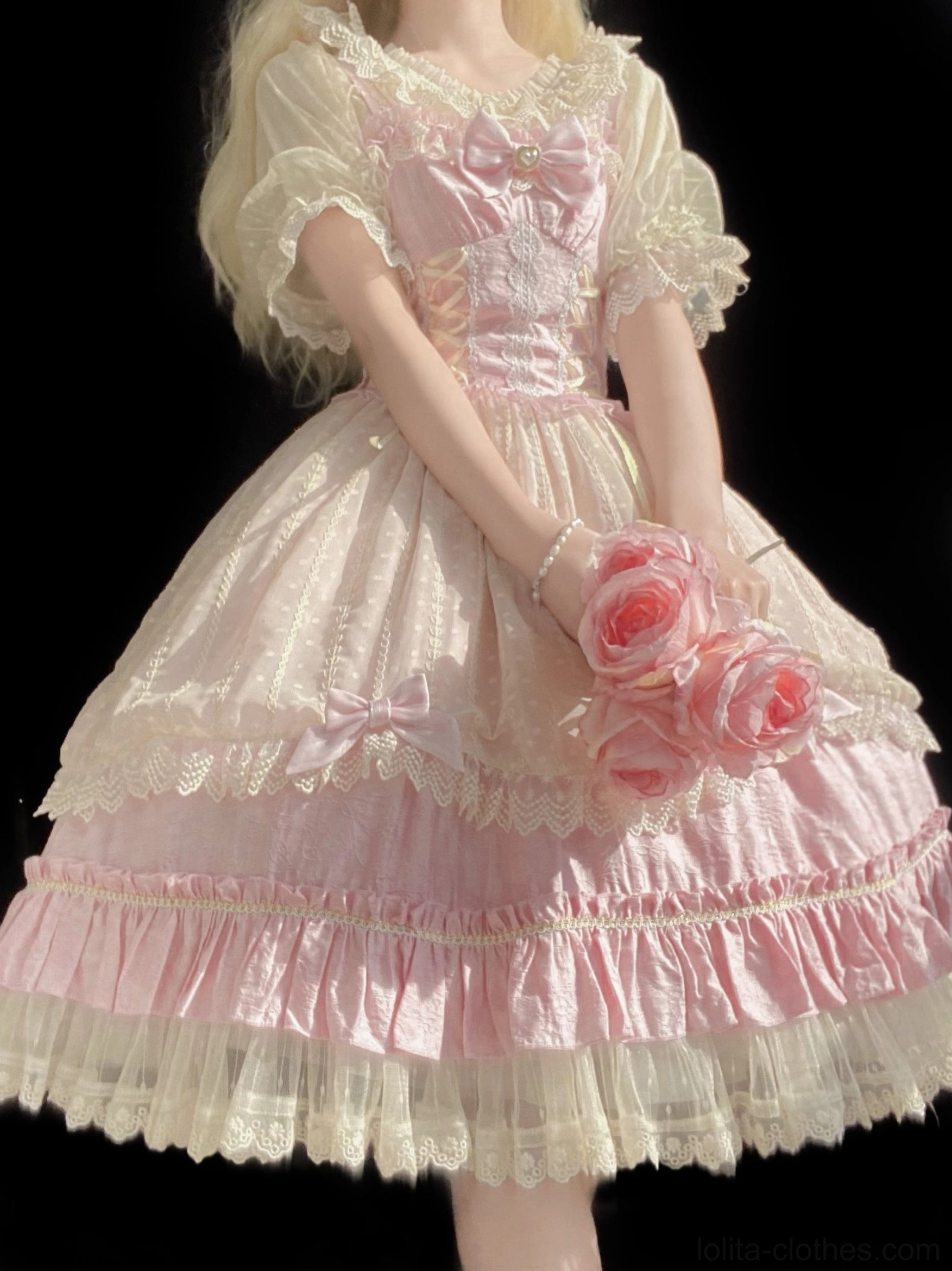Side-front full body view of pink sweet Lolita op dress on model showing tiered ruffled lace skirt, bodice bow decoration, and lace-trimmed puff sleeves