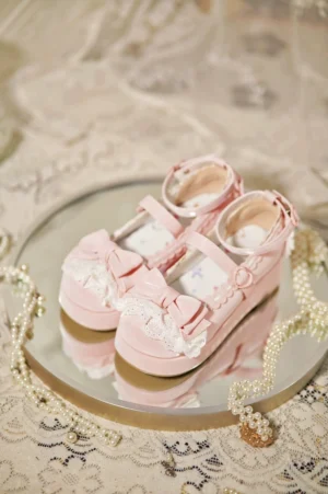 Top-down flat lay view of pink Milky Puff Lolita round-toe wedge heels on round mirror tray with pearl ornaments and vintage lace tablecloth, showcasing ankle strap and bow decoration