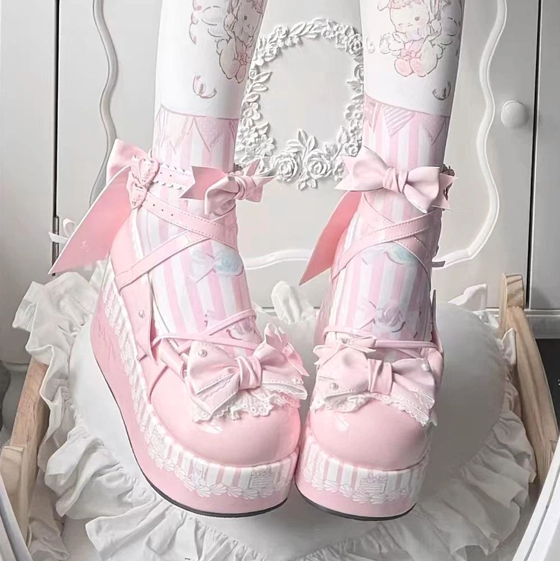 Pink sweet lolita platform Mary Jane shoes with decorative bows and lace details, showcasing rounded toe design and thick wedge sole on ruffled vanity setup with cartoon thigh highs