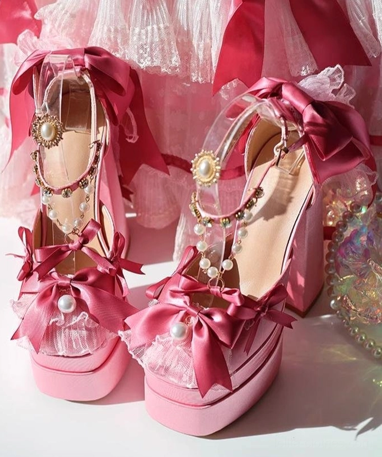 Pair of pink sweet lolita platform shoes displayed on vanity mirror with pearl decorations and rhinestone ankle straps, large back satin bows
