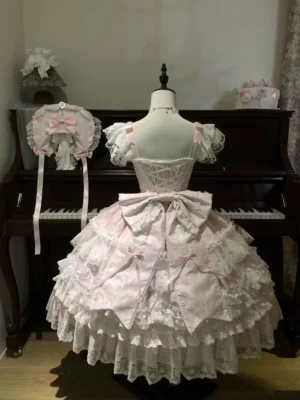 Back view of pink sweet lolita tiered JSK dress showing large detachable waist bow and full layered lace ruffled skirt hem