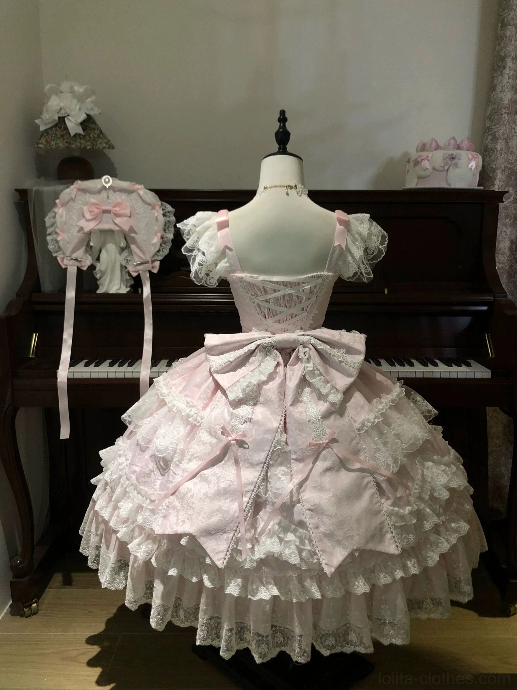 Back view of pink sweet lolita tiered JSK dress showing large detachable waist bow and full layered lace ruffled skirt hem