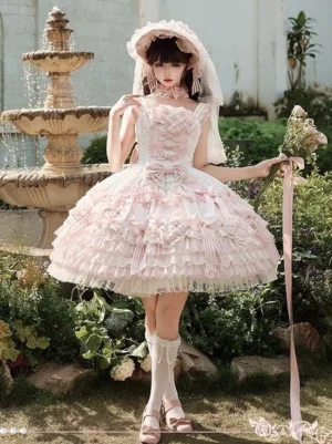 Pink sweet lolita wedding JSK dress full-body front view outdoor garden setting with stone fountain white ruffled lace skirt square neckline bridal veil bonnet